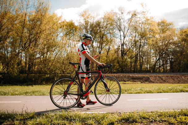 Rowerzysta w kasku i sprawny, cyclocross szkolenia na asfalt drogowy. Mężczyzna sportowiec jeździ na rowerze. Trening na ścieżki rowerowej - Zdjęcie, obraz