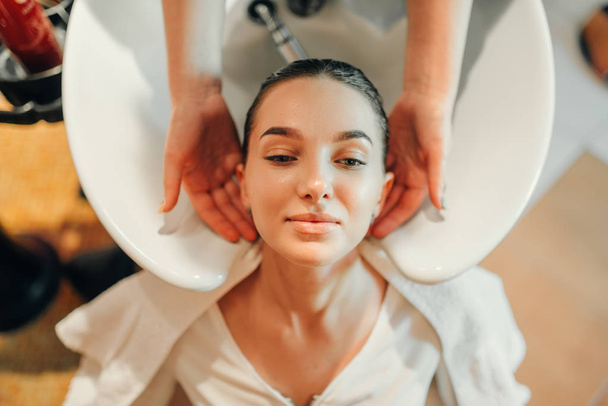 Kampaaja pesee asiakkaan hiukset altaassa, ylhäältä, kampaamo. Ammattimainen hiustenhoito kauneushoitolassa
 - Valokuva, kuva