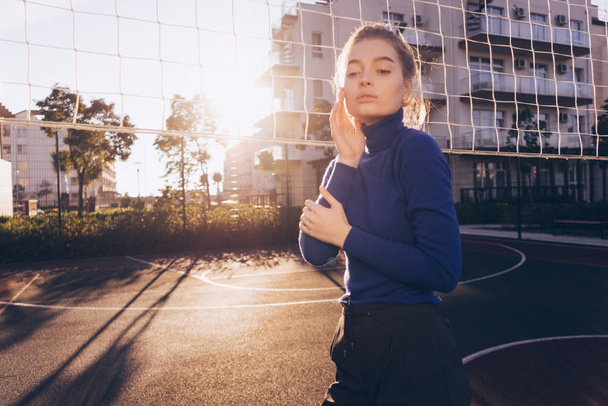 confident beautiful girl model in a fashionable sweater posing on a sports field in the rays of the morning sun - Fotoğraf, Görsel