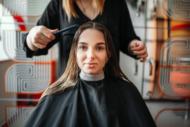 Woman in hairdressing salon, female stylist with scissors and comb in hands on background. Hairstyle making in beauty studio - Photo, Image