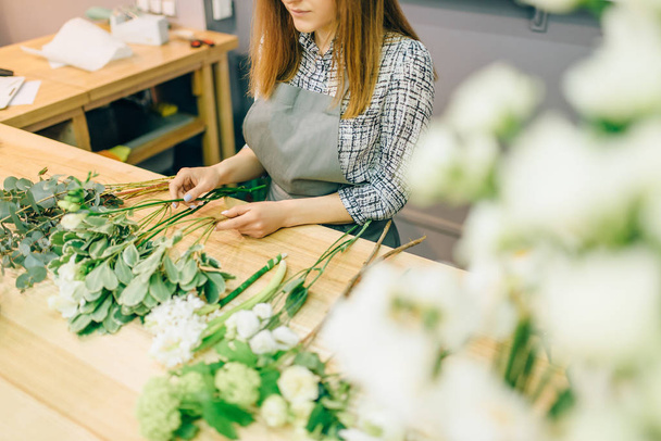 Цветочный букет делает женщина-флористка с пучками растений в руках. Цветочный бизнес, декоративные инструменты
 - Фото, изображение