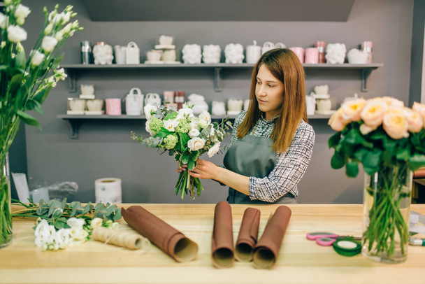 Female florist prepares flower composition, garden equipment on workplace. Flower shop, floral business - Photo, Image