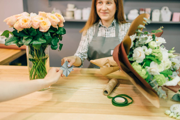 Ανθοπωλείο στη ποδιά δέχεται πληρωμές από θηλυκό πελάτη στην boutique λουλούδι. Floral κατάστημα της επιχειρηματικής ιδέας - Φωτογραφία, εικόνα