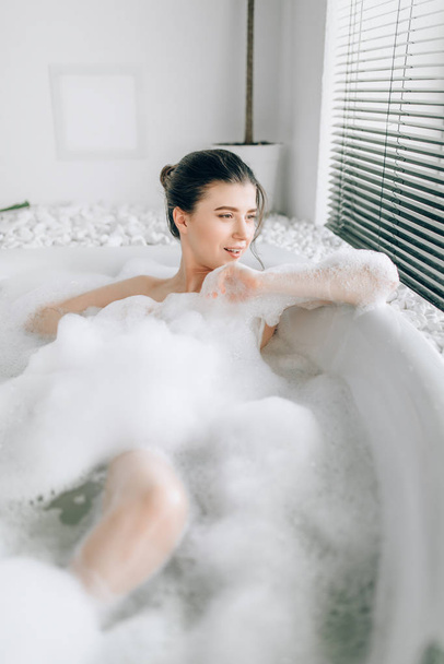 Sexy woman lying in bath with foam, relaxation in luxury bathroom with stone decor - Fotó, kép