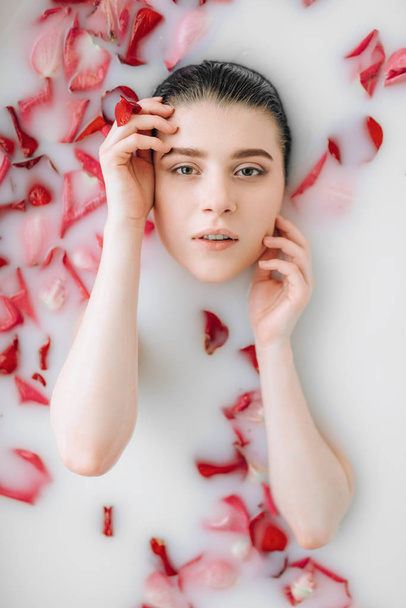 junge Frau liegt in Badewanne mit Schaum und Rosenblättern  - Foto, Bild
