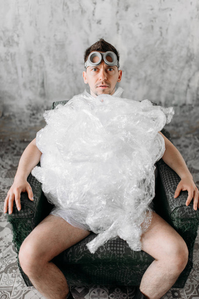 grappige freak man in verpakkingsfolie en Zwemmen goggles, grunge kamer interieur - Foto, afbeelding