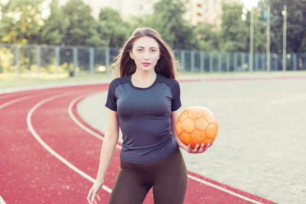 Portret van een mooie jonge vrouw met een bal in haar handen in het stadion. - Foto, afbeelding