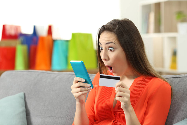 Verbaasd vrouw vinden online creditcard zittend op een bank in de huiskamer houden-aanbiedingen - Foto, afbeelding