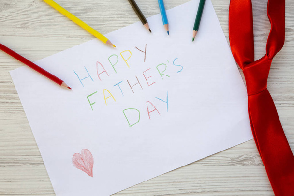 Happy Father's Day inscription with red tie and color pencils on white wooden background. - Photo, Image