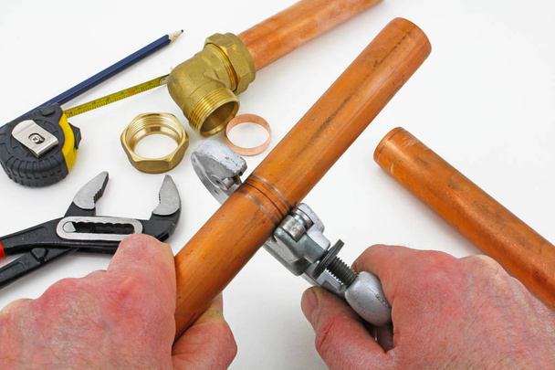 Coupe de tuyau en cuivre Une paire de mains à l'aide d'un coupe-tuyau sur cuivre avec des morceaux de plombier en arrière-plan
 - Photo, image