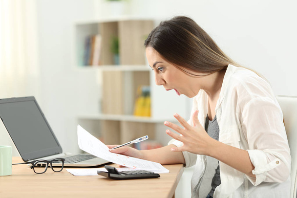 Side view portrait of a surprised woman reading bank statements at home - 写真・画像