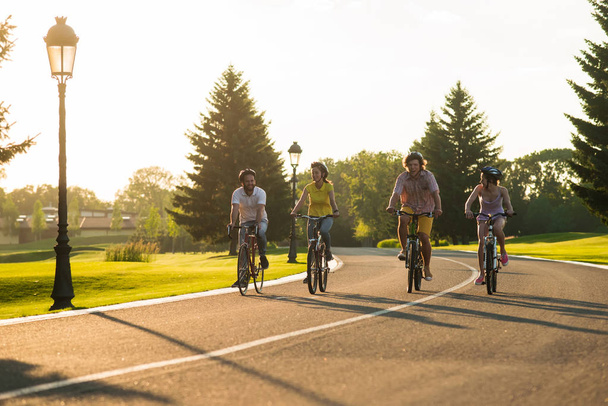 Cute group of friends riding bikes. Happy students cycling on country road. Beautiful nature and sunlight. - 写真・画像