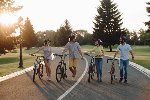 Grupo de ciclistas alegres caminando con bicicletas por el camino
. - Foto, imagen