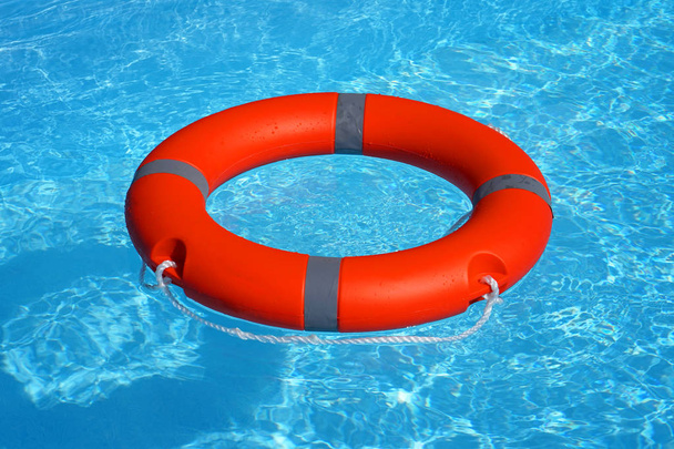Κόκκινο δαχτυλίδι πισίνας ναυαγοσώστη επιπλέει σε μπλε νερό. Δαχτυλίδι ζωής επιπλέει στην κορυφή του ηλιόλουστου μπλε νερού. Δαχτυλίδι ζωής στην πισίνα - Φωτογραφία, εικόνα