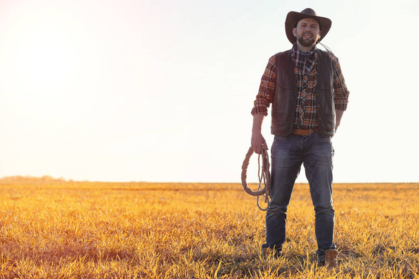 A man cowboy hat and a loso in the field. American farmer in a f - Zdjęcie, obraz