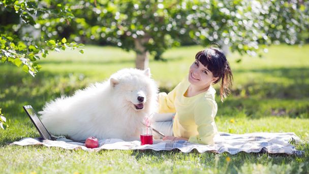 The girl and the big dog lie on the grass in the city park. A brunette girl with a white dog on nature. - Photo, Image