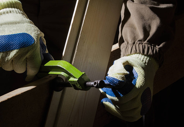 Closeup photo of a worker in outfit with blue gloves using clamp with wooden boards on black background with upper light. - Photo, Image
