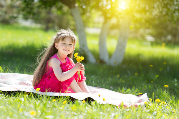 A little girl is holding a bouquet of flowers.A child is sitting on the grass in a park with yellow flowers. - Fotoğraf, Görsel