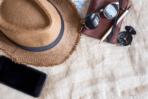 Top view of Summer brown panama straw hat,mobile,sunglasses,notebook map,compass on linen cloth.vacation travel concept.copy space for adding text - Photo, Image