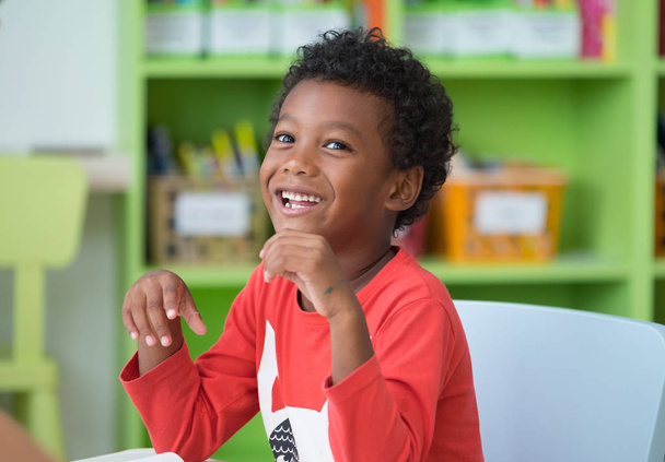 Ragazzo afroamericano di etnia sorridente alla biblioteca nella classe prescolare dell'asilo. Emozioni felici. Concetto di educazione
 - Foto, immagini