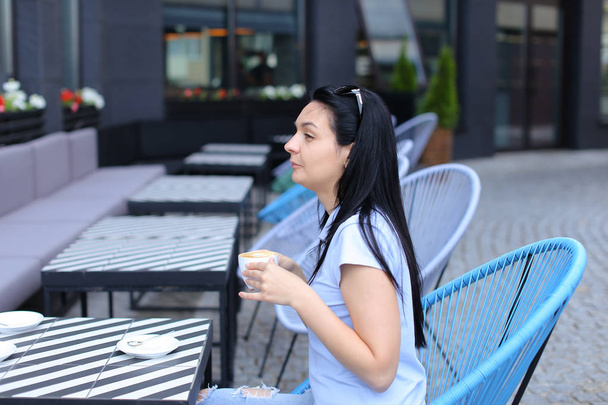 Young brunette woman drinking coffee at cafe and sitting in blue chair. - Photo, Image