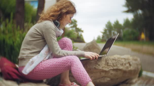 Женщина с ноутбуком отдыхает на скалах в красивом зеленом парке. Молодая постоянная женщина в дендрарии, работающая за ноутбуком. Технологии на открытом воздухе
 - Кадры, видео