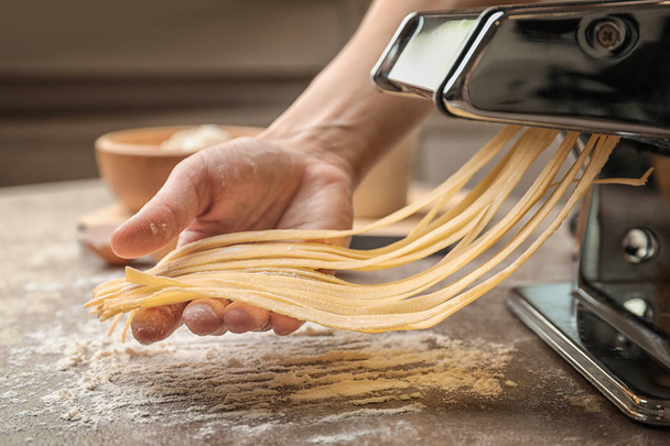 Woman preparing noodles with pasta machine at table - Zdjęcie, obraz