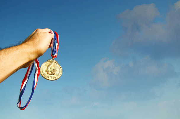 man hand raised, holding gold medal against sky. award and victory concept - Фото, зображення