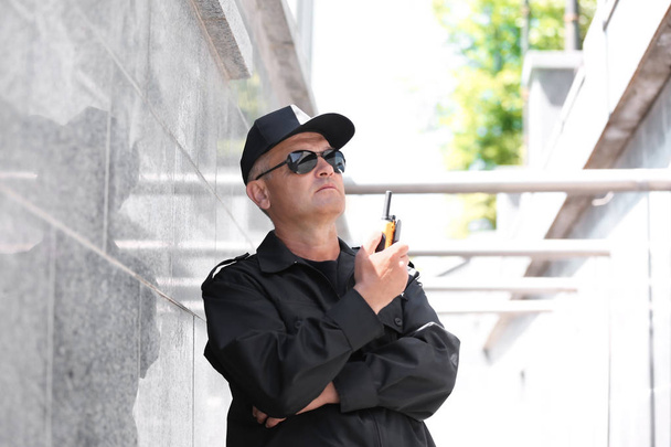 Male security guard using portable radio transmitter outdoors - Foto, imagen