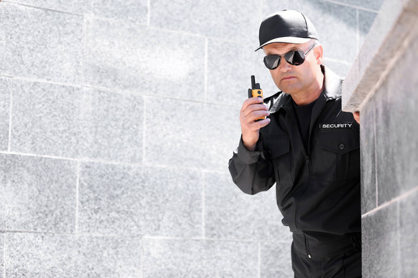 Male security guard using portable radio transmitter outdoors - Foto, imagen