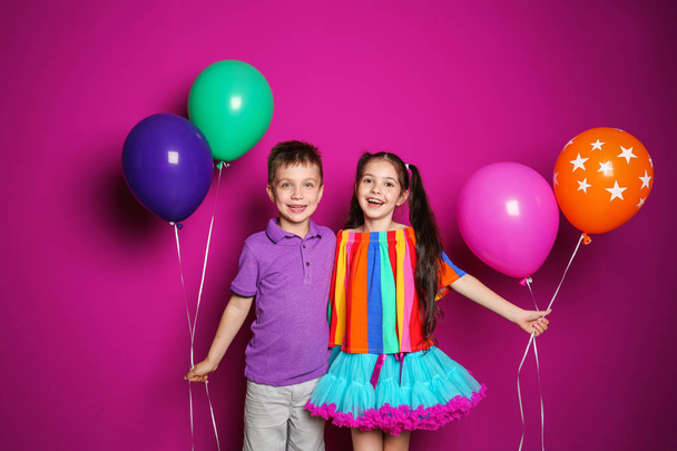 Cute girl and boy with balloons on color background. Birthday celebration - Foto, imagen