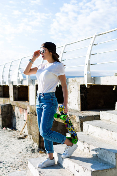 Mooie yound vrouw met een skateboard op een strand - Foto, afbeelding
