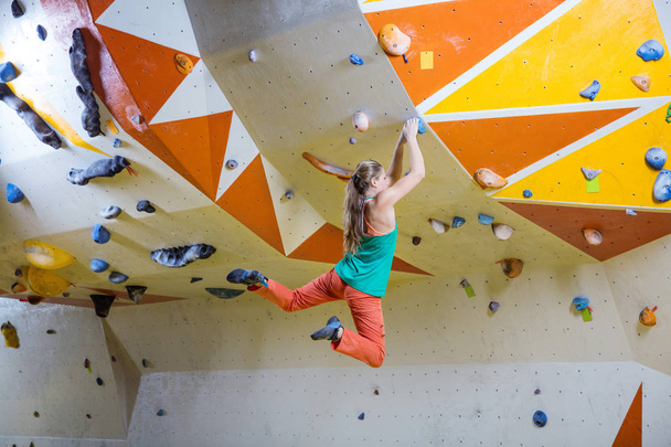 junge athletische Frau springt in Boulderhalle auf Handgriff - Foto, Bild