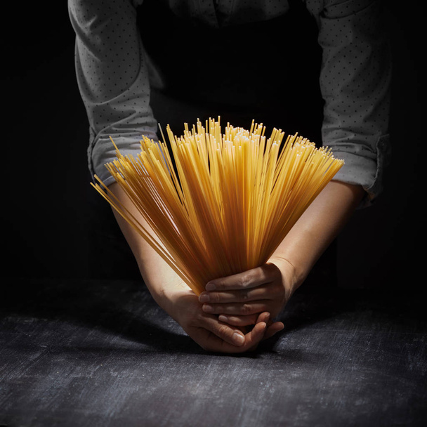 bunch of spaghetti in hands of woman on dark background,  concept of Italian food - Фото, изображение