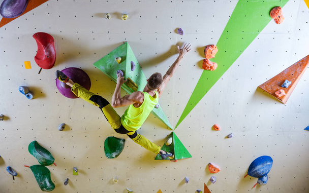 Young man climbing bouldering route, doing splits to reach next handhold. In indoor climbing gym. - Photo, Image