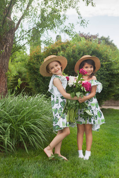 Portrait of smiling beautiful girls with bouquet of peonies against green grass at summer park. - Foto, Bild