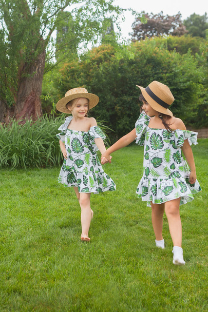 Portrait of smiling beautiful girls with hats against green grass at summer park. - Фото, изображение