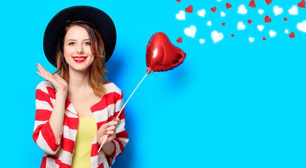 Muotokuva nuori hymyilevä punatukkainen valkoinen eurooppalainen nainen hattu ja punainen raidallinen paita sydämen muotoinen lelu sinisellä taustalla sydämet
 - Valokuva, kuva