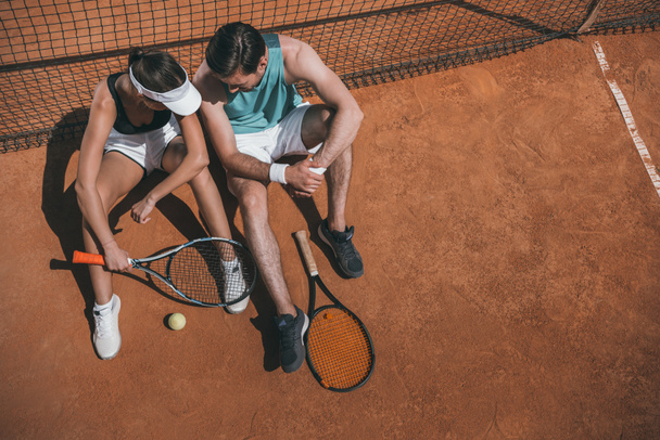 Blick aus der Vogelperspektive auf ein junges Paar, das sich am Netz zurücklehnt und sich auf dem Tennisplatz entspannt - Foto, Bild