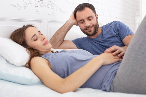 Comfort in tummy. Positive pregnant woman lying on back while man looking at her - Photo, image