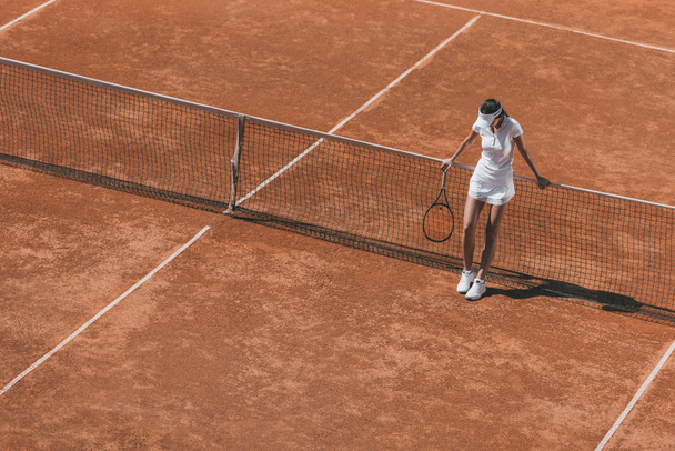 high angle view of woman relaxing on tennis court after match and leaning back on net - Photo, Image