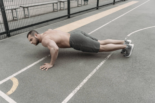 Jóképű félmeztelen férfi során push a sportpálya - Fotó, kép