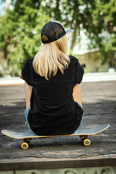 夏の日のスケート ボードで彼女の背中に黒の t シャツの女の子が座っています。 - 写真・画像