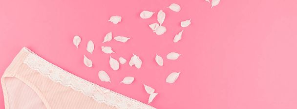 Feminine flat lay set of female panties and white flowers petals on pastel pink color background for fashion blog and social media with copy space for text. Long wide banner - Foto, imagen