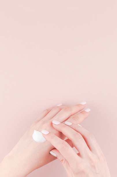Creative image of woman moisturizing her hand with cosmetic cream lotion with copy space on millennial pink background in minimalism style. Concept template feminine blog, social media, beauty concept - 写真・画像