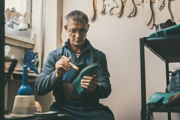 Der gestandene Schuhmacher hält Stiefelwerkstück und arbeitet mit Sohle in seiner traditionellen Werkstatt - Foto, Bild