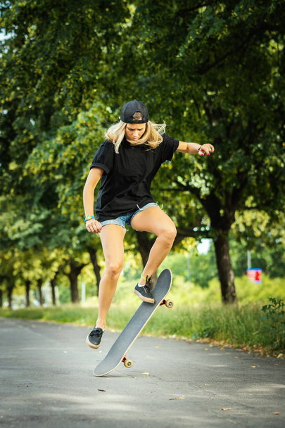 Mädchen mit Mütze führt an einem Sommertag einen Skateboard-Trick auf - Foto, Bild