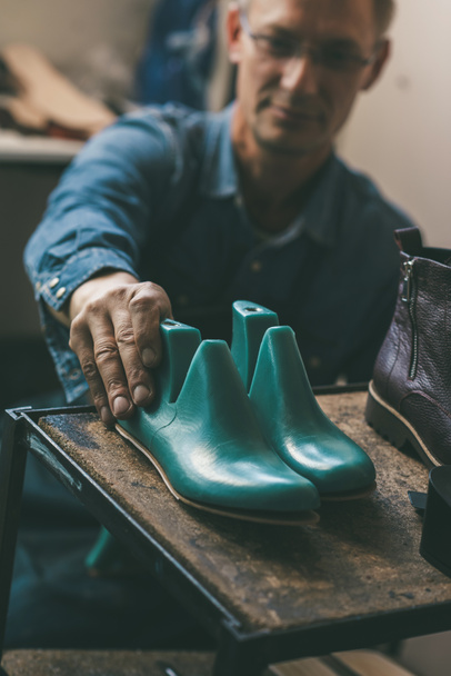 selective focus of shoemaker holding footwear workpieces from shelf in workshop - Photo, Image