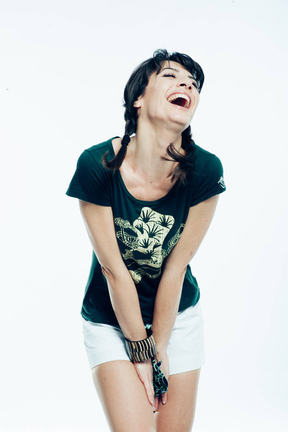 Jonge Kaukasische brunette met staart haar plezier in de studio. Witte achtergrond, groene shirt gekleed. Kopiëren van ruimte - Foto, afbeelding