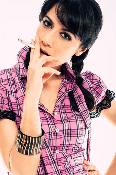 Joven morena caucásica con peinado de cola fumando un cigarrillo. Blanco fondo de estudio de tiro. Camisa rosa vestida
 - Foto, imagen